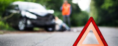 Warning triangle in the foreground with a damaged car in the blurred background.